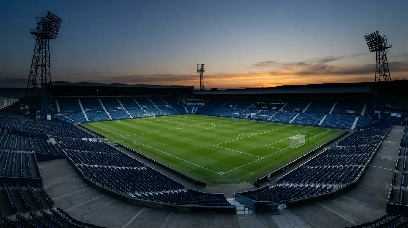 An empty football stadium with floodlight masts at dusk